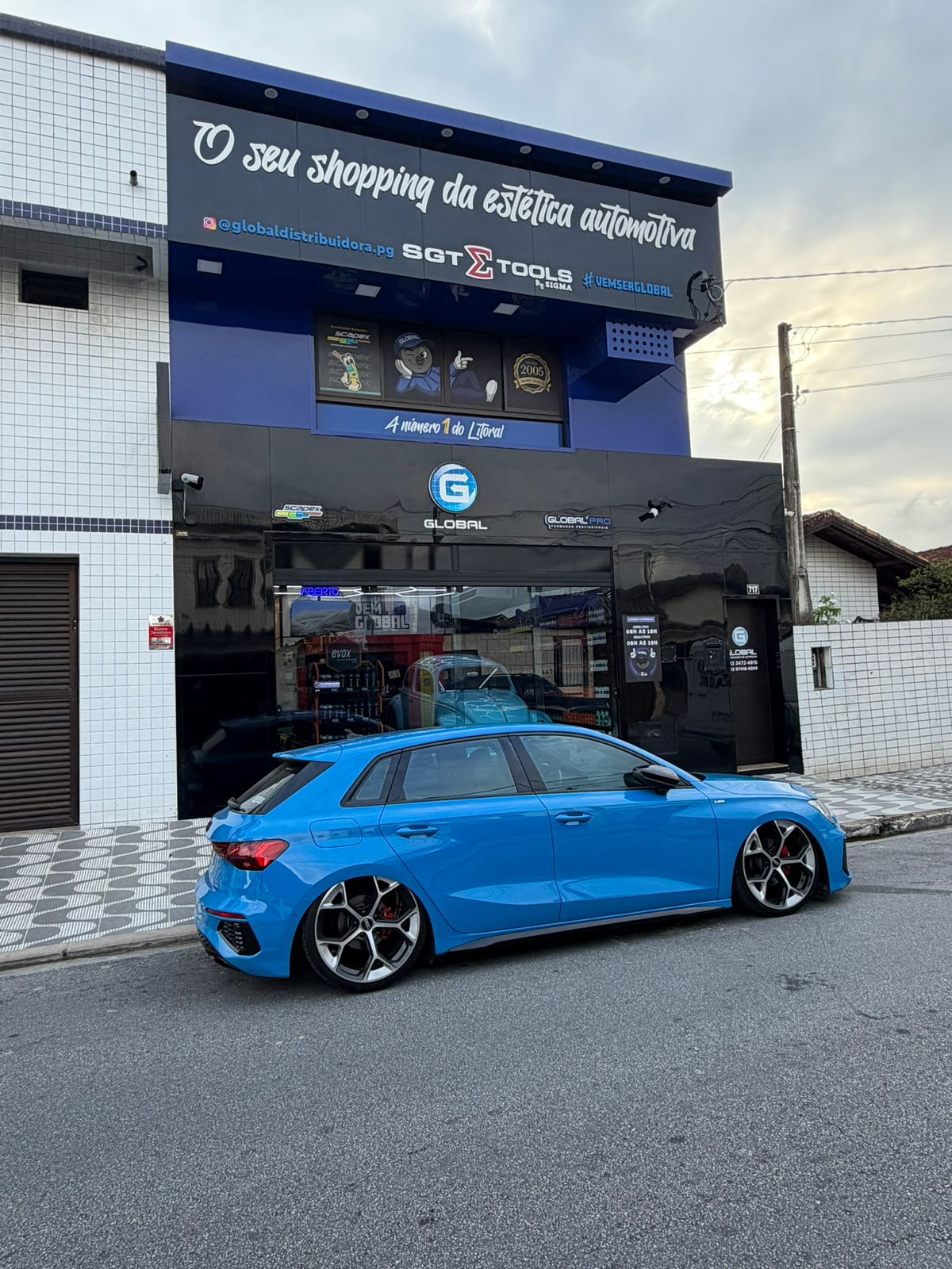 Fachada da loja Global Distribuidora em Praia Grande, com um carro azul estacionado em frente